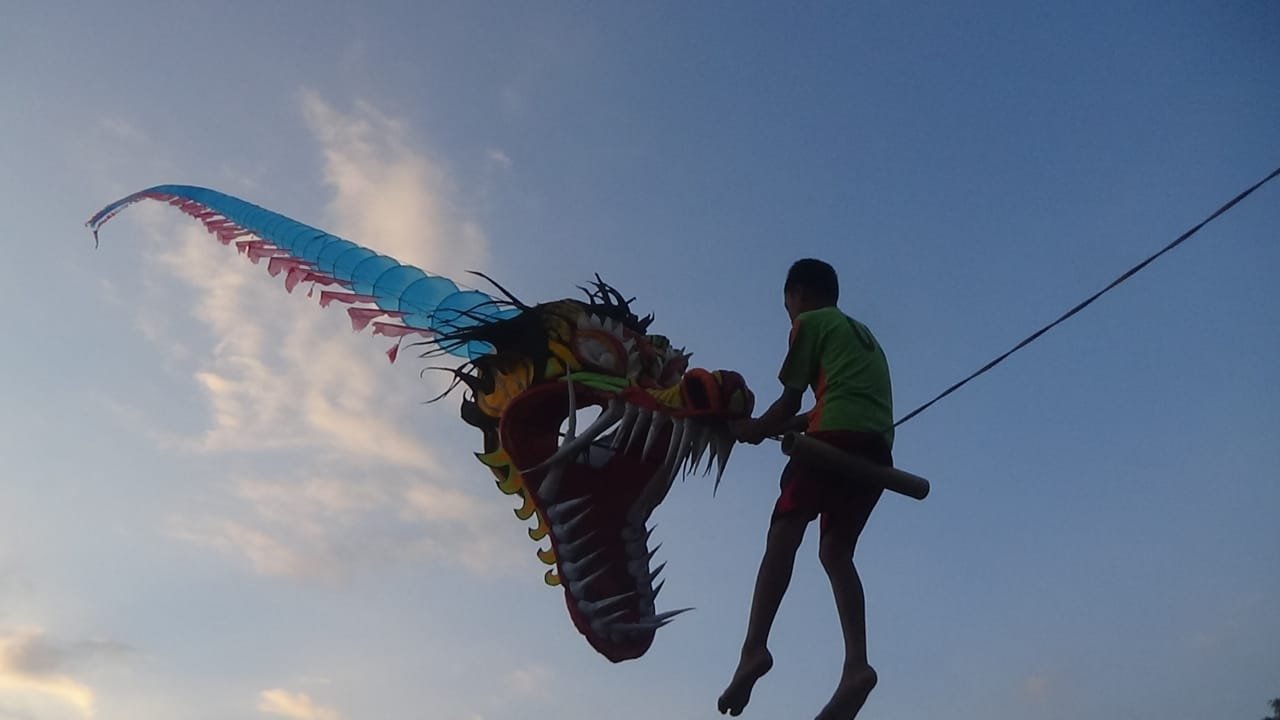 TERBANG. Seorang anak di Jenar Kidul tampak antusias menaiki layang-layang naga dengan ukuran raksasa. (Foto lukman)